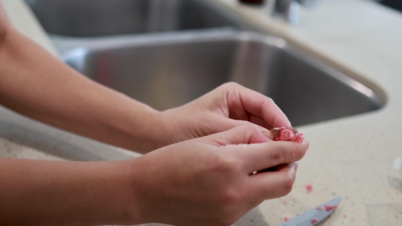 Hands delicately extract caviar from finger lime in a well-lit kitchen environment, showcasing culinary preparation