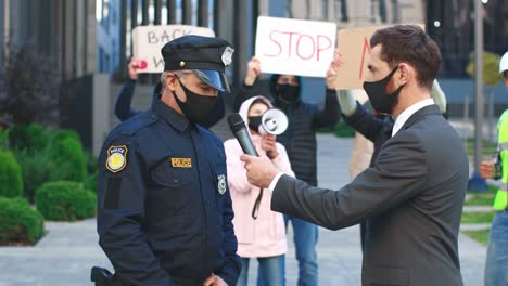 periodista o corresponsal caucásico con máscara protectora en una entrevista con un policía en una protesta contra el covid 19