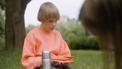 Close-up-view-of-a-blonde-boy-sitting-in-the-park.-He-is-making-a-paper-plane