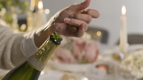 close up of person opening bottle of champagne at table set for meal at wedding reception