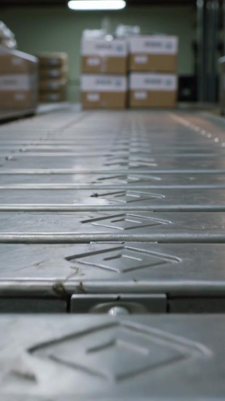 Vertical video: Starting conveyor moving diamond plate carrying pallets in warehouse for shipping