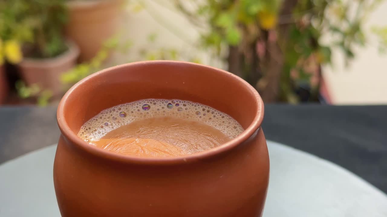Primo piano statico di tè caldo in tazza di argilla, leggera schiuma sulla superficie, calda luce solare con una leggera sfocatura del giardino che crea un'atmosfera rilassante, calma e serena!!!