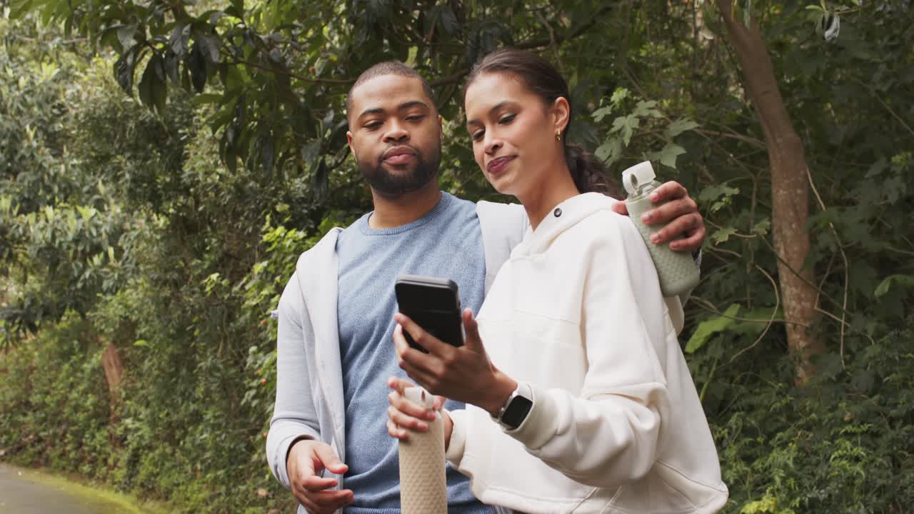 Strolling onto park path, Couple pulling smartphone and holding water bottle posing for selfie