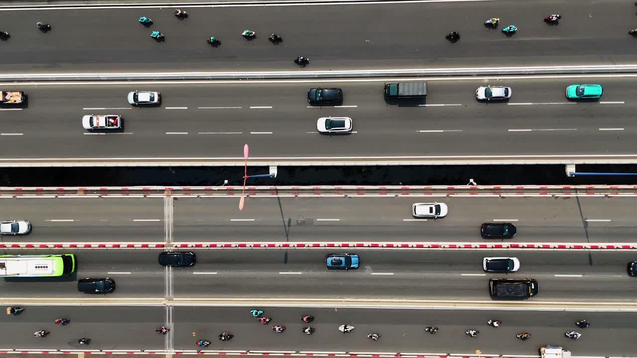 Top-down drone shot of busy traffic on a multi-lane highway in Ho Chi Minh City, Vietnam. Motorbikes, cars, and trucks move along the bridge spanning the Saigon River.