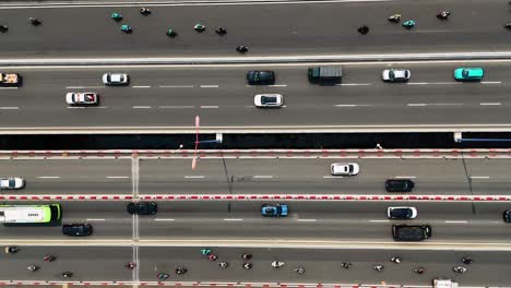 Top-down drone shot of busy traffic on a multi-lane highway in Ho Chi Minh City, Vietnam. Motorbikes, cars, and trucks move along the bridge spanning the Saigon River.