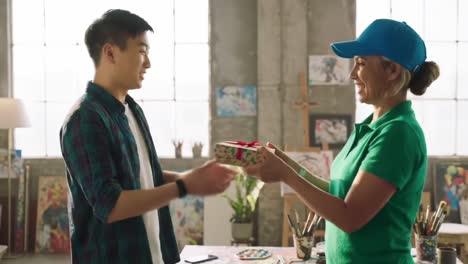 a joyful exchange in an artistic studio: a young man receives a colorful gift from a smiling artist in vibrant surroundings filled with creativity