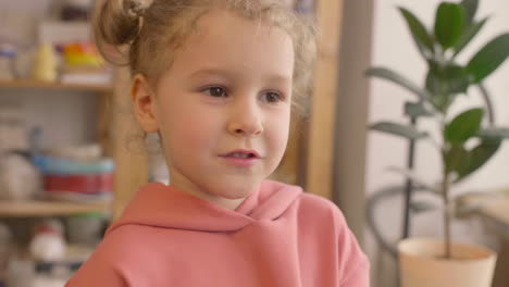 Close-Up-View-Of-Blonde-Little-Girl-Smelling-Lilac-Flowers-In-A-Craft-Workshop