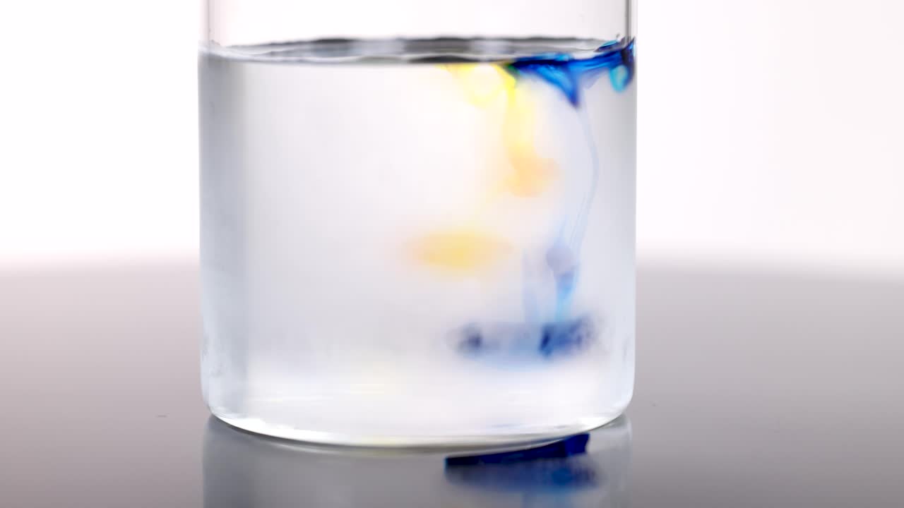 Blue and yellow dye swirl in clear cold water under bright studio lighting