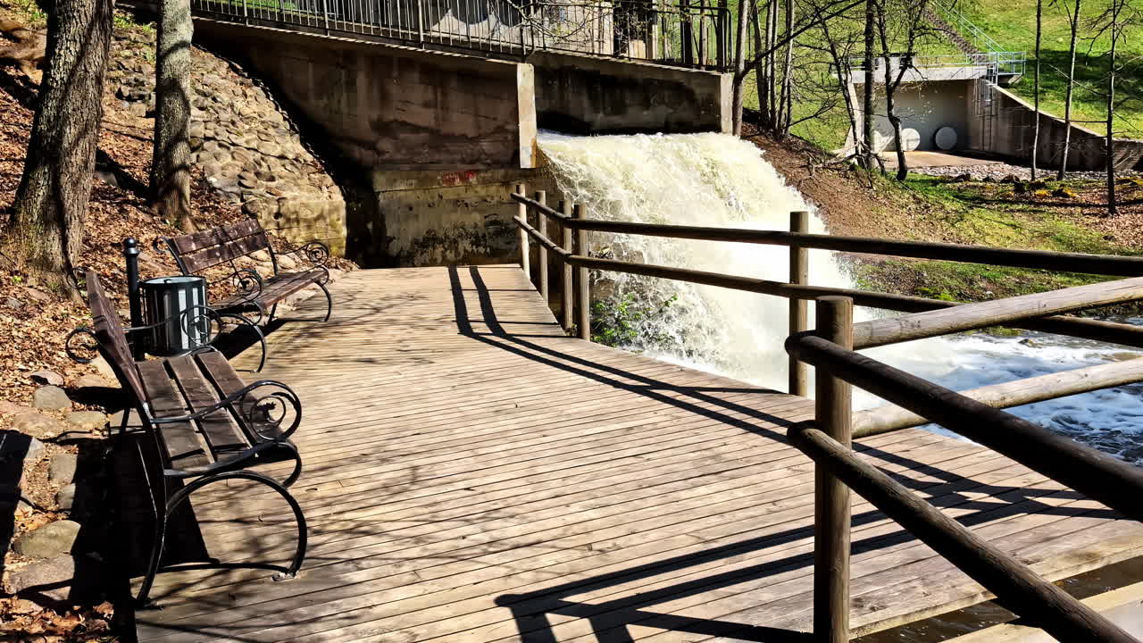 Wooden terrace with benches overlooking dam waterfall in Smiltene on Abuls river