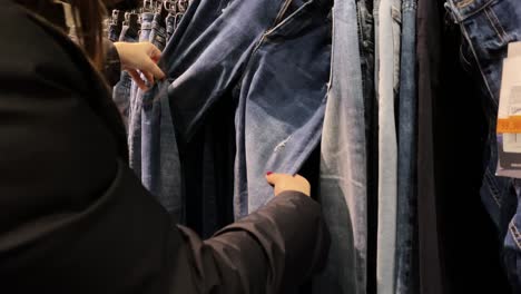 Close-up The girl is looking through her denim pants in the store. Slow motion