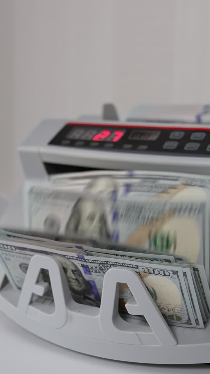 Little money counting machine turning money. Laptop with a black screen and a curve at backdrop in blur. Vertical video