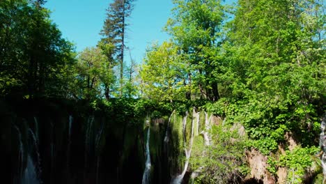 Drone-ascent-over-waterfalls-focusing-on-a-large-turquoise-blue-lake-in-a-Croatian-national-park