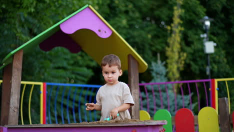 peaceful little boy plays in the sandbox playing with sand. calm toddler kid pays outdoors moving sand with the shovel.