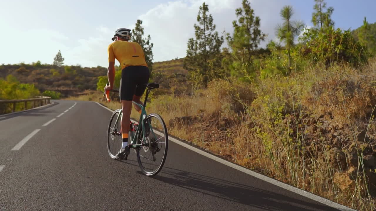 Engaging in outdoor exercise, a man cycles on a quiet morning road with his road bike. The slow-motion recording highlights the excitement of extreme sports
