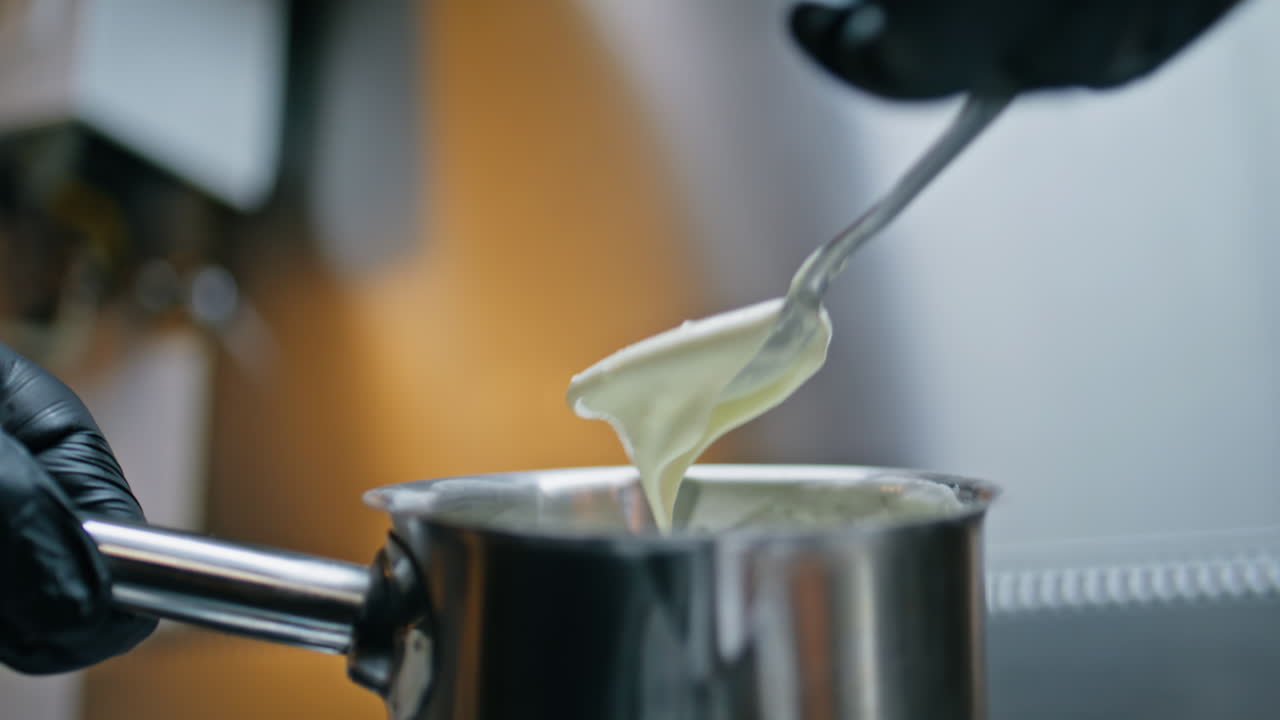 Chef spoon taking sauce from metal pan checking consistency at kitchen closeup