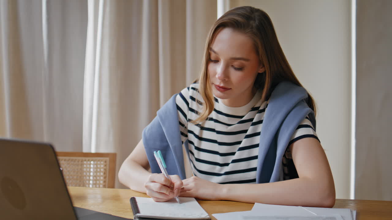 Serious woman planning project writing in notebook at home workplace closeup