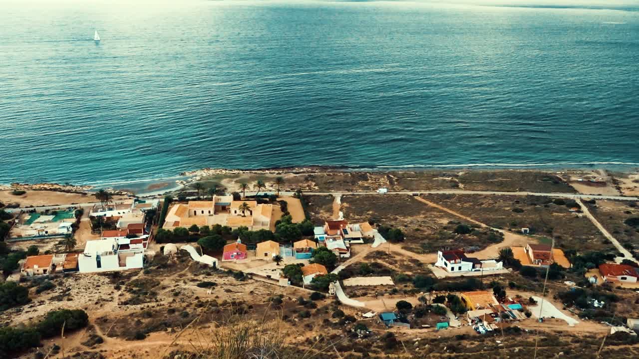 mirando hacia abajo a un pueblo desde lo alto de los acantilados de santa pola: edificios en primer plano con un telón de fondo de agua azul