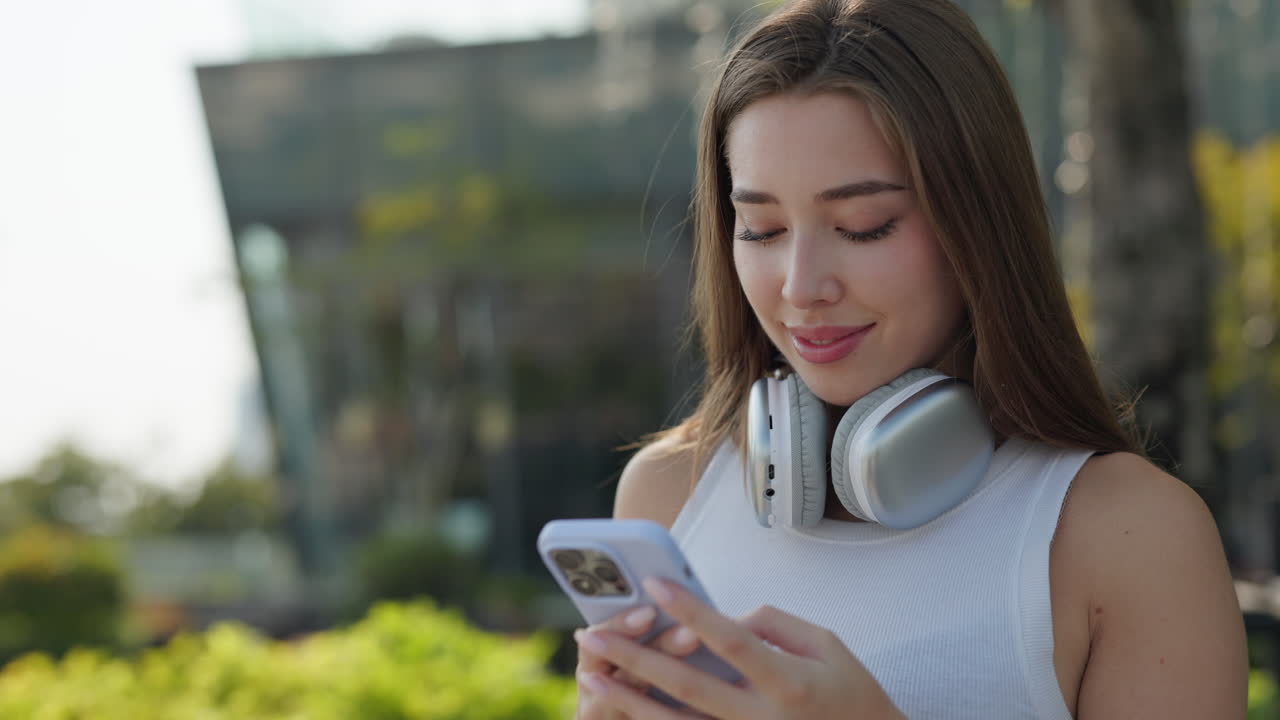 Woman using smartphone outdoors with headphones around neck