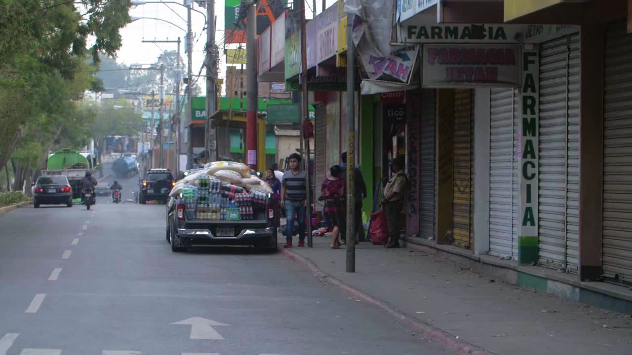 Slow motion street view of overloaded vehicle with large rice bags and soda bottles parked street side in Zone 18 Guatemala City - handheld camera