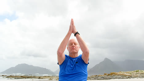 vista frontal de un anciano caucásico meditando en la playa 4k