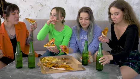 girl friends drinking beer, eating pizza and laughing on a sofa