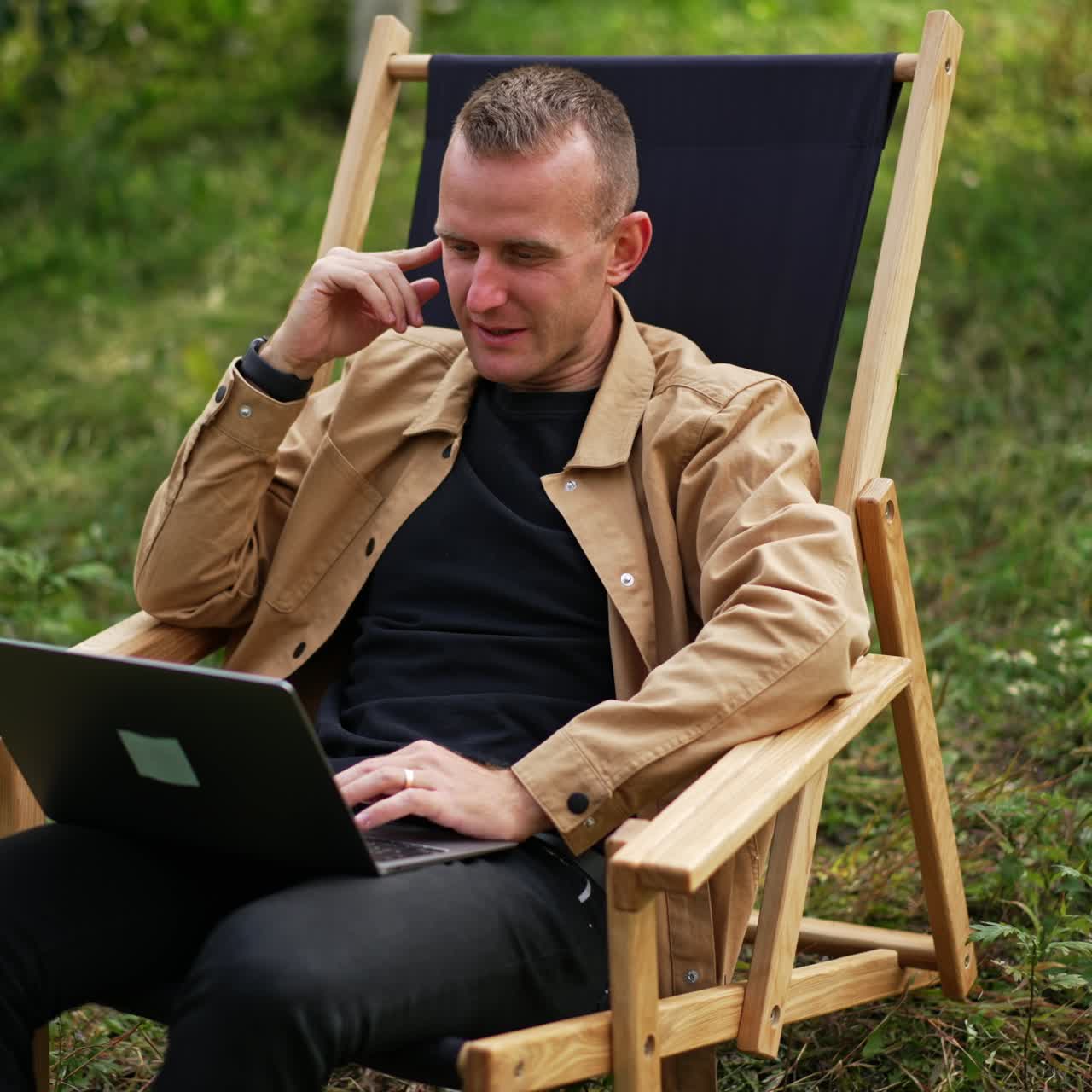 Positive laughing man working remotely having online conversation. Freelance specialist doing his job far from office in the nature