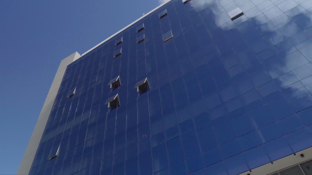 vista panorámica de un edificio espejado que refleja el cielo azul con nubes