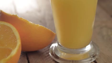 glass of fresh orange juice with cut oranges on wooden background