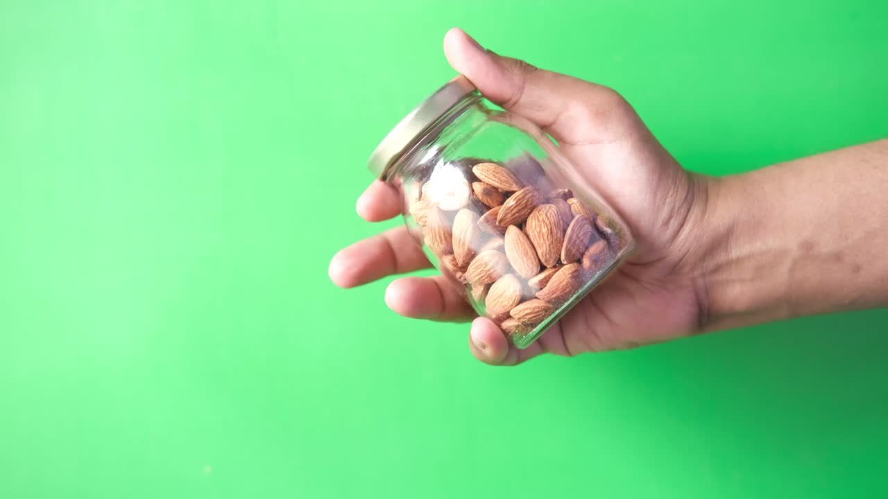 sosteniendo una botella de nueces de almendra contra un fondo verde
