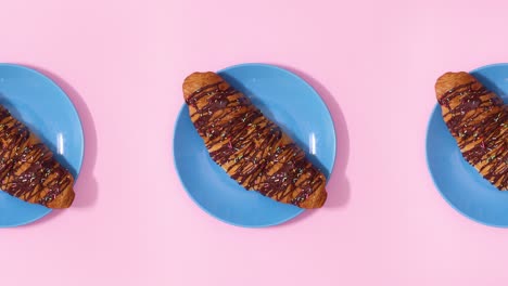 three fresh delicious croissants rotate on blue plate on pink theme. stop motion