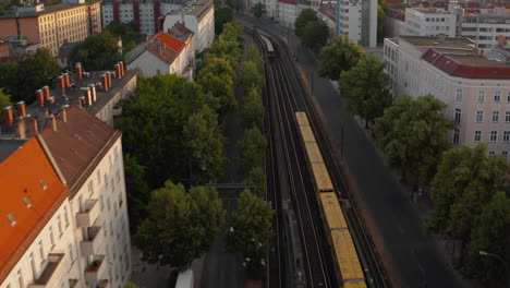 Aerial-morning-view-of-two-trains-passing-by-each-other.-Forwards-flying-above-wide-street-with-Sbahn-line-tracks.-Berlin,-Germany