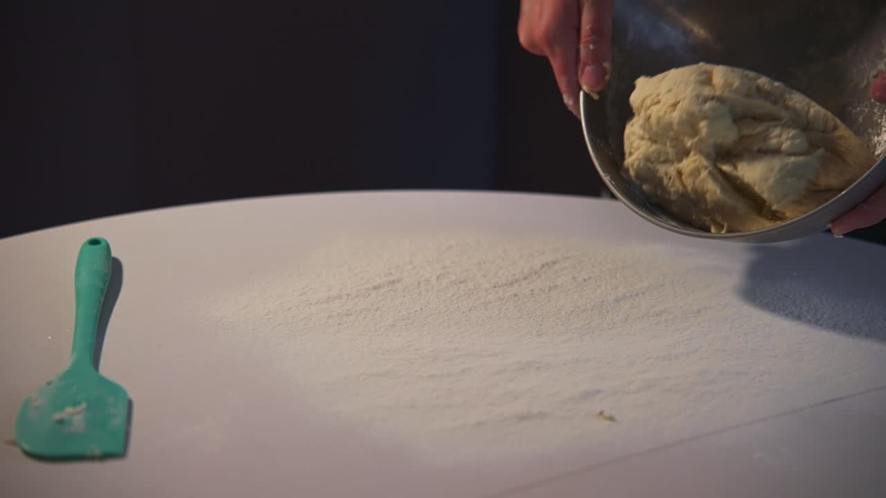 Mani che versano impasto fresco da una ciotola su un tavolo infarinato