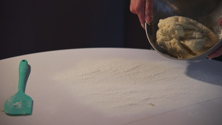Mani che versano impasto fresco da una ciotola su un tavolo infarinato