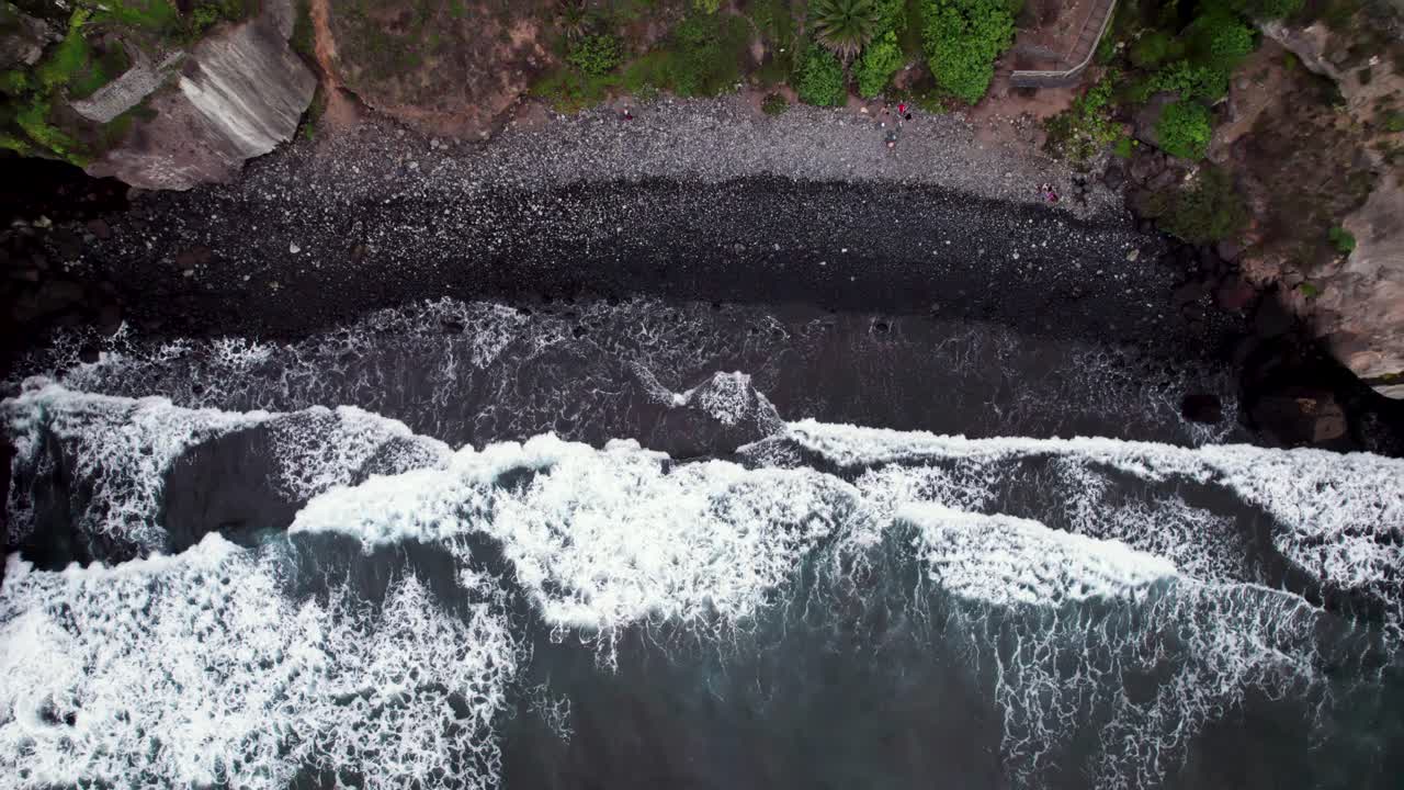 Aerial top down view of black sand beach wave in a rocky coastal bay
