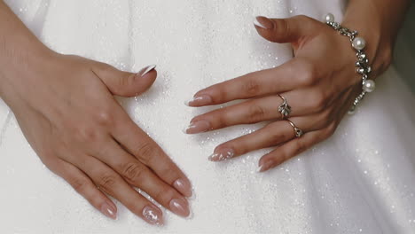 bride in shining dress shows hands with rings and bracelet