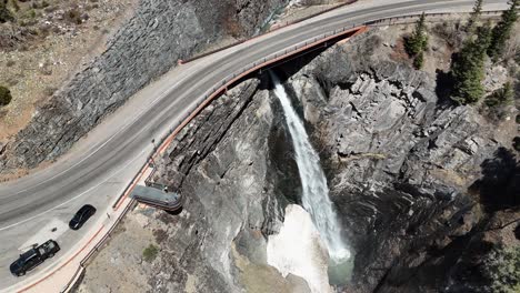 drone slowly panning around a large waterfall while tourists look from afar