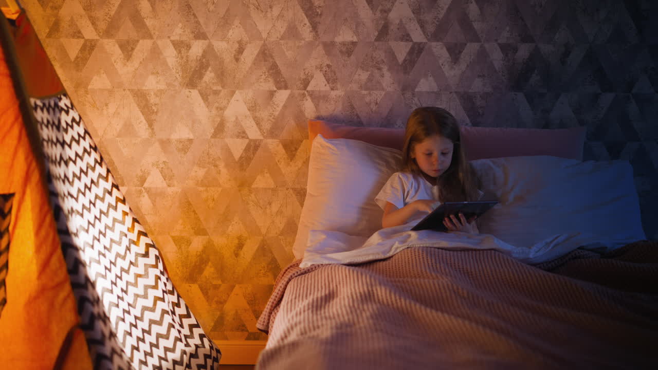Pretty child plays game online via tablet in shady room