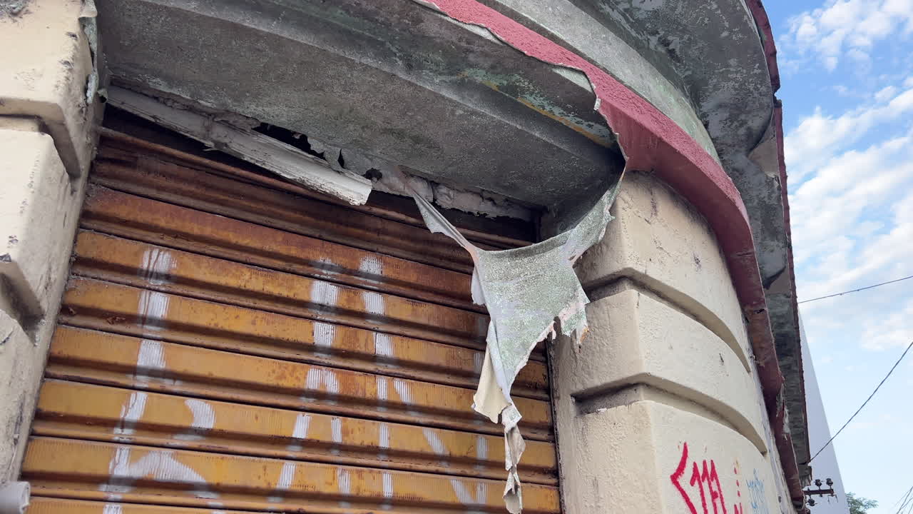 Primo piano di pittura scrostata e facciata rovinata dalle intemperie con serranda metallica, macchie e segni di graffiti.