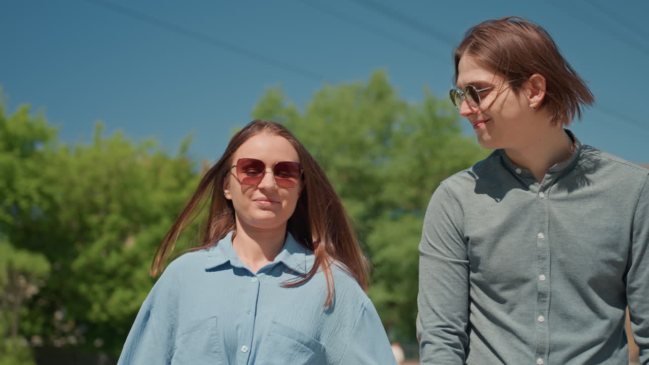 Una pareja alegre pasea por una zona verde soleada, charlando animadamente mientras pasean a su labrador por un sendero exuberante. Esta pareja relajada comparte sonrisas y bromas mientras explora un vibrante parque en un día soleado.