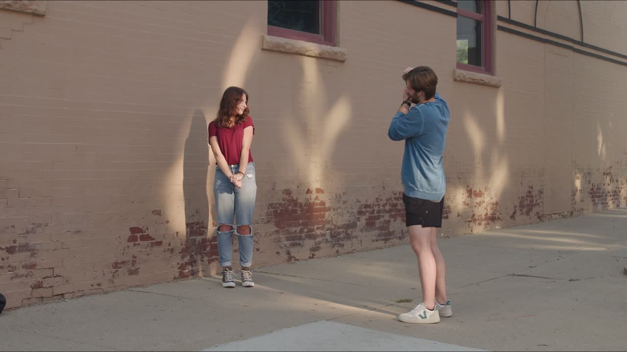 Man photographs woman against a brick background