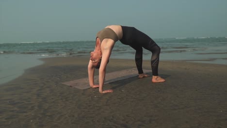 bridge asana yoga position, woman on a beach stretching setu bandha sarvangasana