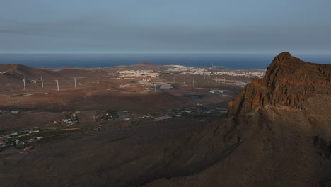 aerial panorama revealing roque aguayro and wind turbines silhouetted against sunset colors over gran canaria volcanic landscape