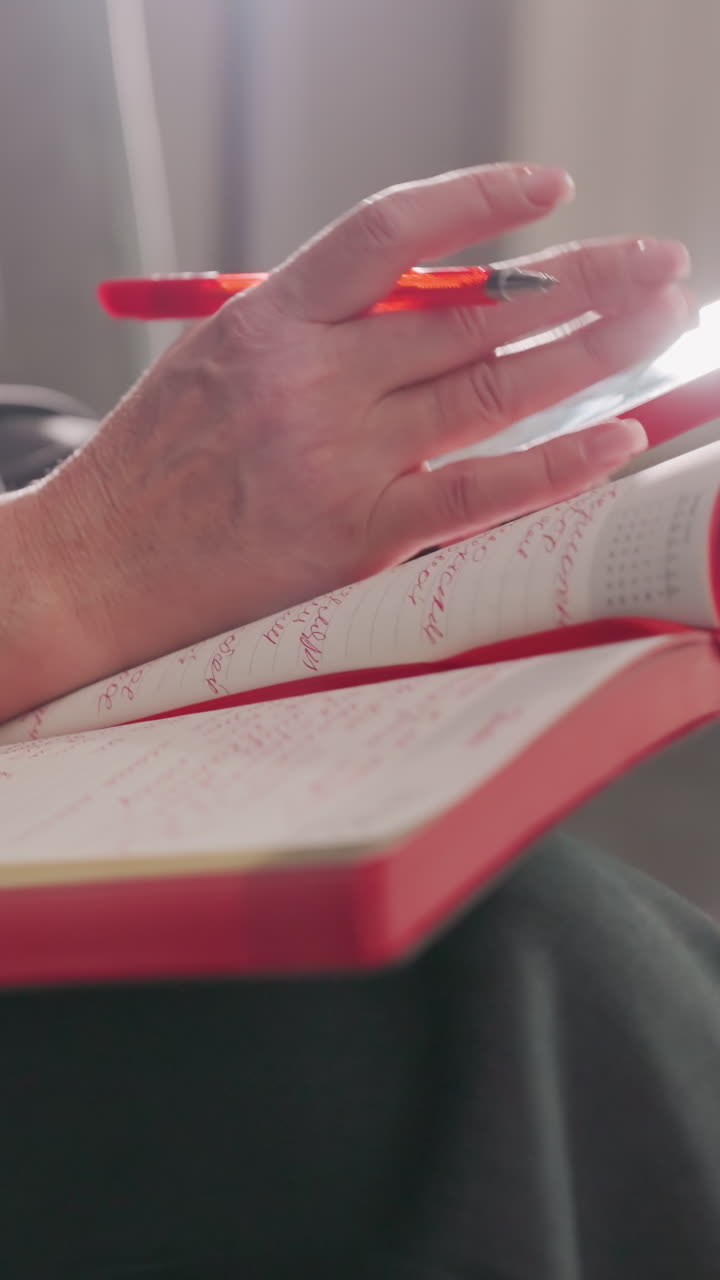 Businesswoman writing in red notebook with pen, focused on work, modern office environment, gray suit, sitting relaxed, productivity, decision-making, corporate workspace, concentration