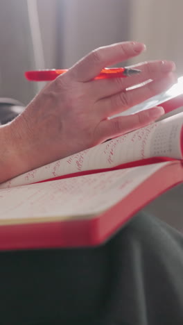 businesswoman writing in red notebook with pen, focused on work, modern office environment, gray suit, sitting relaxed, productivity, decision-making, corporate workspace, concentration