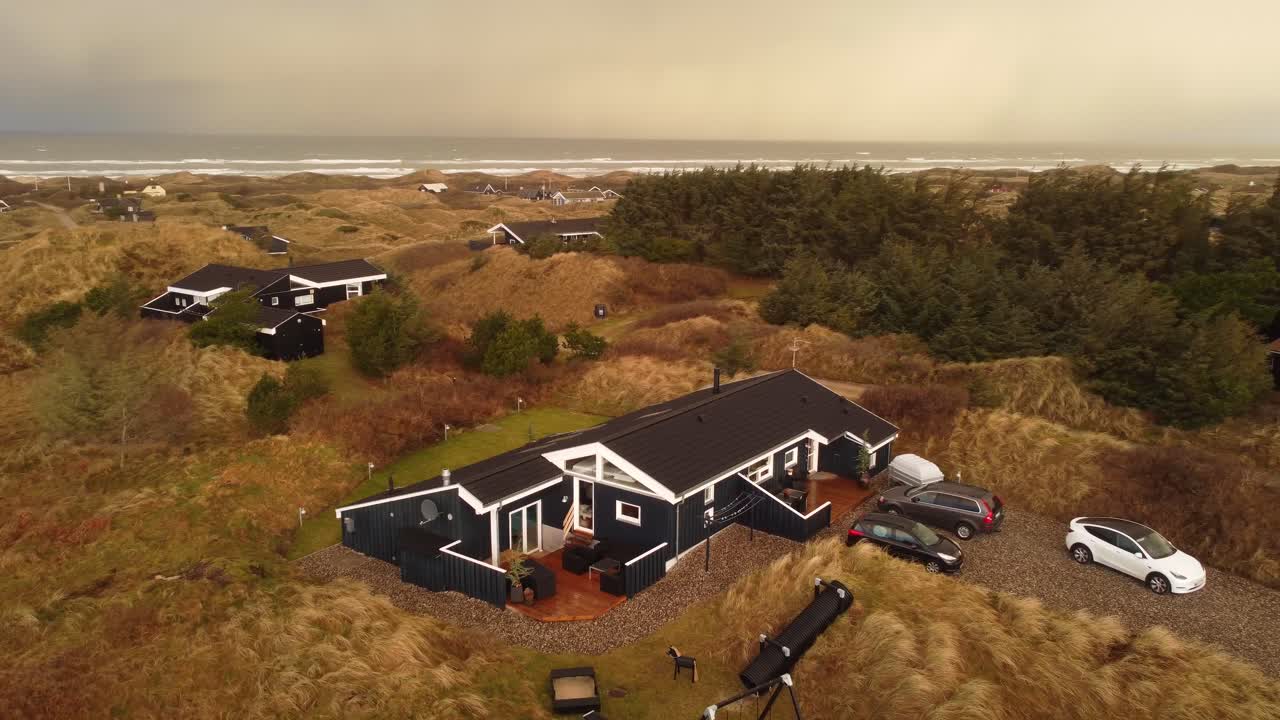 Moderne sort-hvidt sommerhus på landet ved havet, med cirkulær droneoptagelse