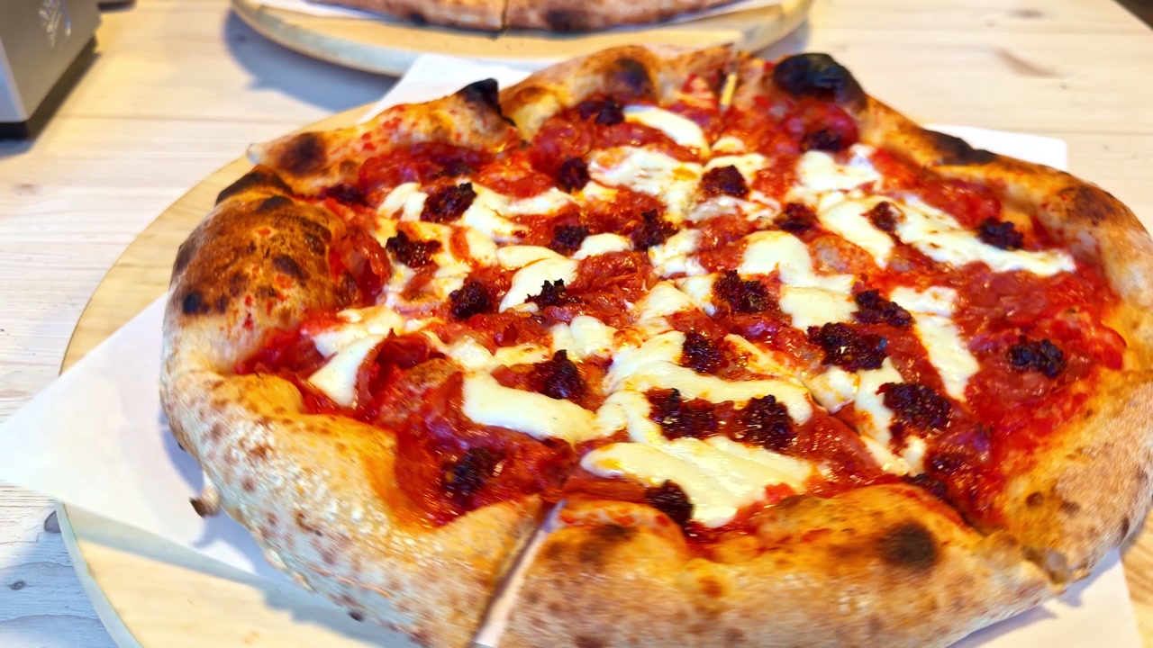 Rotating view of gourmet Neapolitan pizza featuring crispy crust with tomato sauce and fresh white cheese toppings on round board