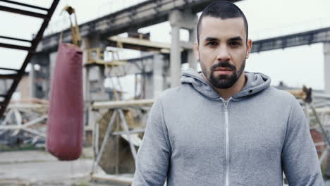 handsome bearded sportsman looking with serious expression at the camera outdoors an abandoned factory on a cloudy morning