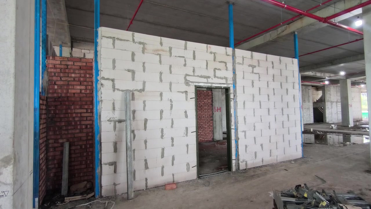 Installazione di una parete in blocchi di calcestruzzo aerato autoclavato (CAA) in un cantiere edile. Presenta rinforzi e architravi metallici per l'efficienza strutturale. Le moderne tecniche di muratura accelerano l'avanzamento della costruzione.