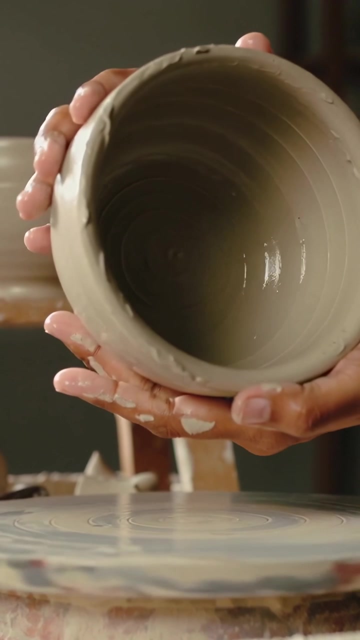 Video verticale: Mani di vasaio che sollevano e controllano una ciotola di argilla in studio mentre la ruota rallenta per la rifinitura