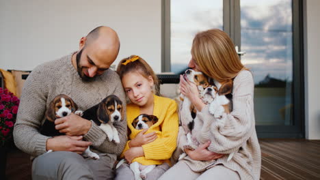 una familia feliz está sentada en la puerta de su casa, jugando con los cachorros. mamá papá y su hija